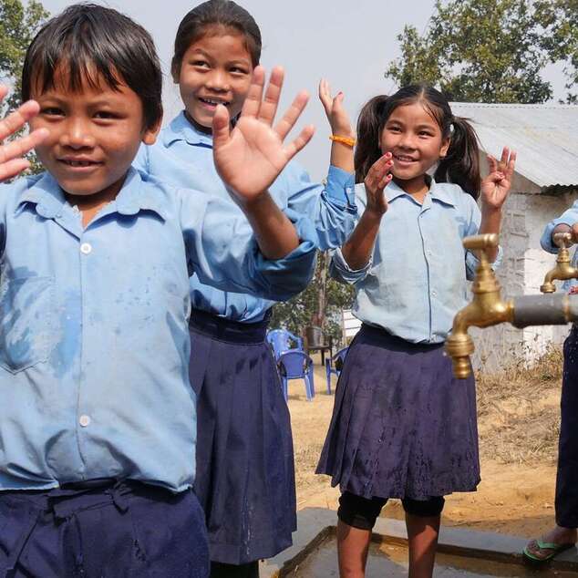 WASH-Projekt in Nepal: Kinder stehen winkend vor Wasserhähnen.