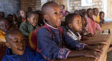Fröhliche Kinder sitzen auf Schulbänken und schauen Richtung Tafel