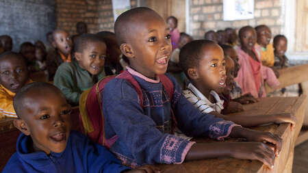 Fröhliche Kinder sitzen auf Schulbänken und schauen Richtung Tafel