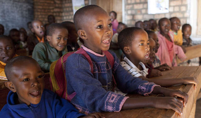 Fröhliche Kinder sitzen auf Schulbänken und schauen Richtung Tafel