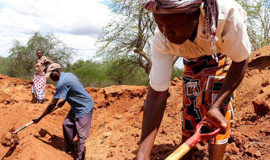 Männer und Frauen graben auf einem Feld.