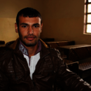 Junger Mann blickt in die Kamera und sitzt in der Schule