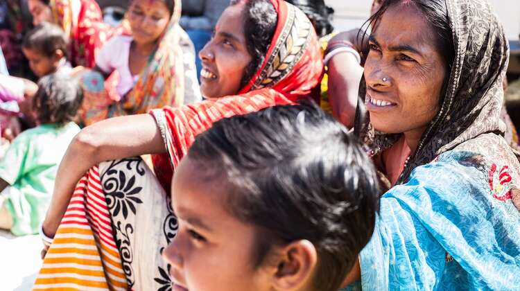 Frauen im traditionellen Sari sitzen auf dem Boden und lachen.
