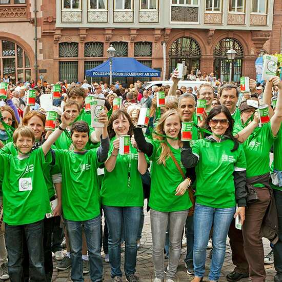 Menschen mit grünen T-Shirts schauen lachend in die Kamera.