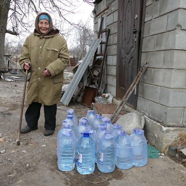 Eine Frau steht neben Wasserkanistern, Ukraine 2022.