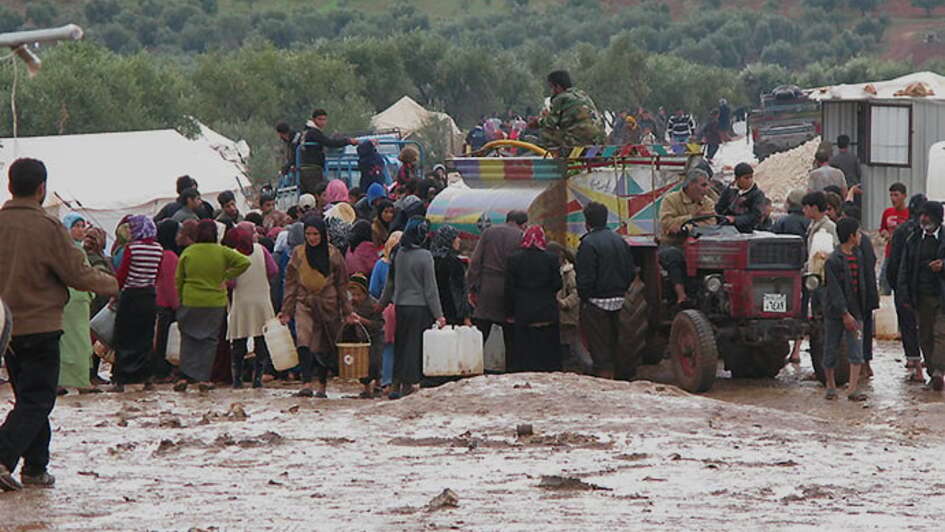 Viele Flüchtlinge stehen vor einem LKW, der sie mit Wasserkanistern versorgt.rhalten.
