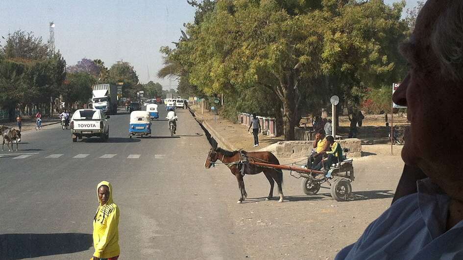 Straße mit regem Verkehr in Addis Abeba. Zu sehen sind Autos, Menschen und ein Kutsche.