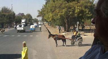 Straße mit regem Verkehr in Addis Abeba. Zu sehen sind Autos, Menschen und ein Kutsche.
