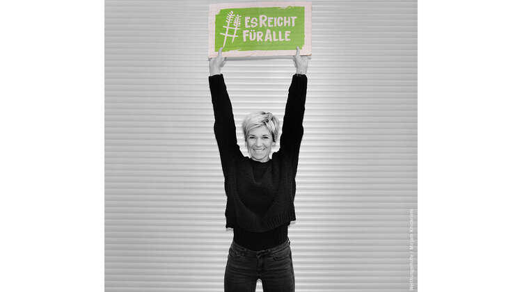 Schauspielerin Kerstin Landsmann hält ein Schild mit dem Welthungerhilfe-Hashtag #EsReichtFürAlle über den Kopf.