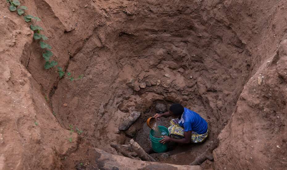 Eine Frau schöpft Wasser in einem tiefen Loch.