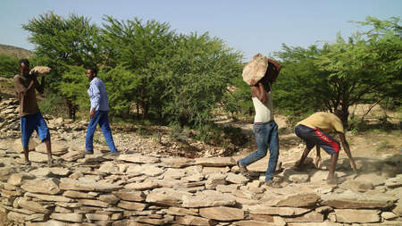 Männer tragen Steine und bauen einen Damm