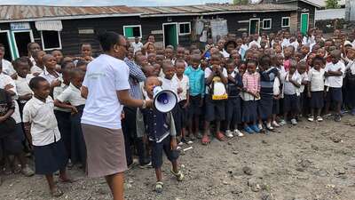 Ein Schüler sagt etwas durch ein Megafon, im Hintergrund viele weitere Schüler.