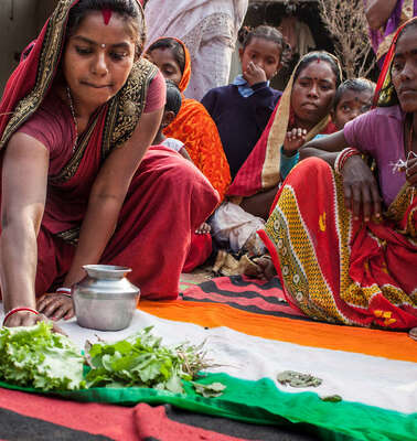 Eine Frau in einem Sari hockt auf dem Boden, vor ihr eine indische Flagge. Sie schiebt einen Salat auf den grünen Teil der Flagge.