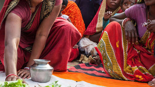 Eine Frau in einem Sari hockt auf dem Boden, vor ihr eine indische Flagge. Sie schiebt einen Salat auf den grünen Teil der Flagge.