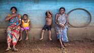 Zwei Frauen in Indien sitzen in traditionellen Gewändern mit Kindern auf dem Dorfplatz.