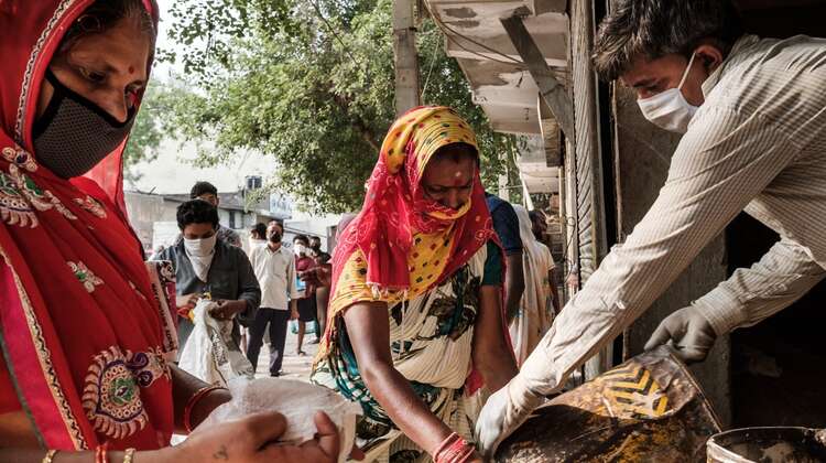 Frauen mit Maske verteilen Lebensmittel, Indien.