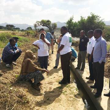 Mehrere Personen stehen und sitzen an einem Bewässerungskanal.