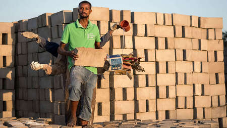 Drei Männer stehen hintereinander und strecken die Arme aus, in jeder Hand halten sie einen Rohstoff zur Herstellung von Ziegeln aus Abfallstoffen.