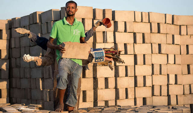 Drei Männer stehen hintereinander und strecken die Arme aus, in jeder Hand halten sie einen Rohstoff zur Herstellung von Ziegeln aus Abfallstoffen.