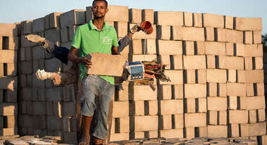 Drei Männer stehen hintereinander und strecken die Arme aus, in jeder Hand halten sie einen Rohstoff zur Herstellung von Ziegeln aus Abfallstoffen.