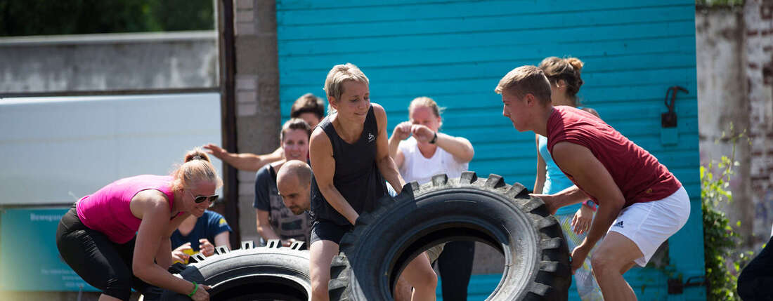 Menschen in Sportklamotten rollen große Reifen.