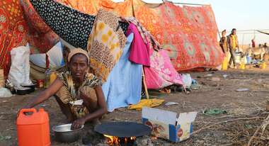 Eine Frau bereitet eine Mahlzeit zu, im Hintergrund sieht man eine provisorische Unterkunft. Foto: WFP
