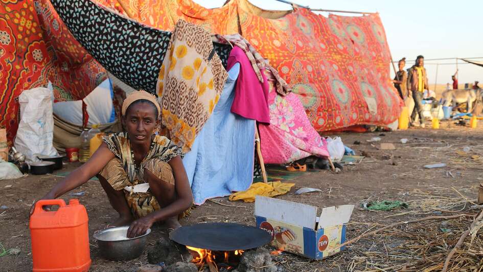 Eine Frau bereitet eine Mahlzeit zu, im Hintergrund sieht man eine provisorische Unterkunft. Foto: WFP