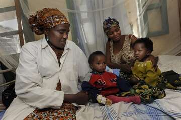 Zwei Kinder und zwei Frauen sitzen auf einem Bett im Krankenkaus