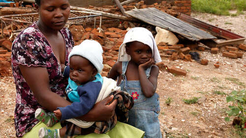 Eine Mutter sitzt mit ihren zwei Kindern vor ihrem zerstörten Haus