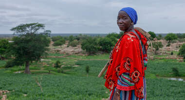 Eine Frau in farbenfroher Kleidung steht mit einem landwirtschaftlichen Werkzeug auf einem Feld in Mali.