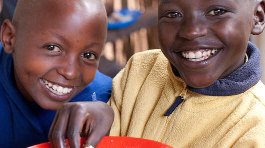 Regelmäßig spenden: Kinder in Burundi mit gefüllten Tellern bei der Verteilung von Schulmahlzeiten