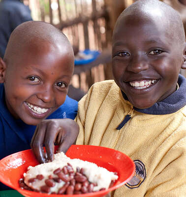 Regelmäßig spenden: Kinder in Burundi mit gefüllten Tellern bei der Verteilung von Schulmahlzeiten
