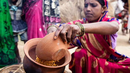 Eine Frau im Sari mit einem Ton-Gefäß in der Hand, das gefüllt ist mit Essen.