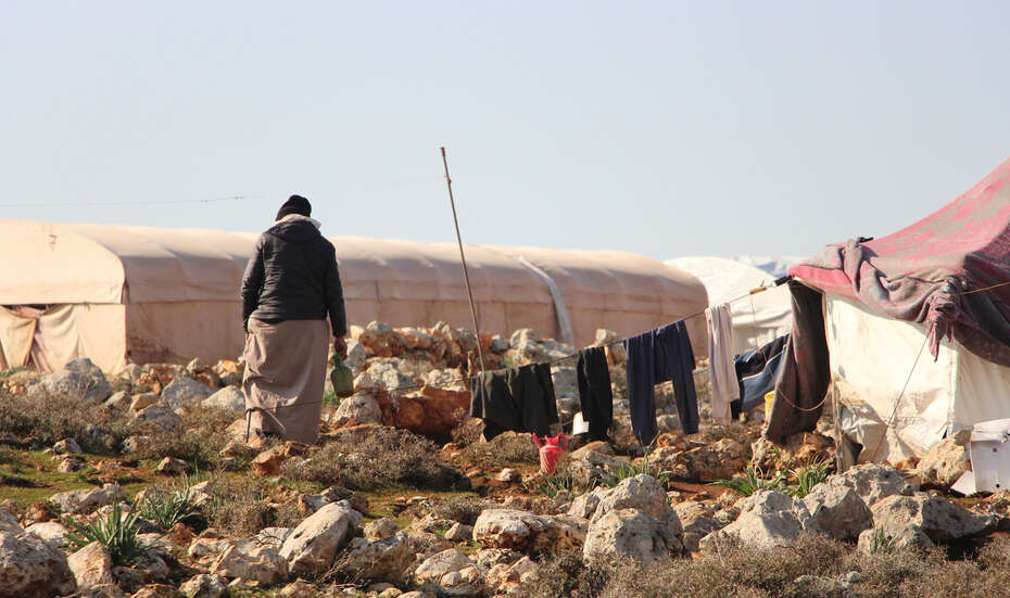 Eine Person von hinten. Sie geht durch ein Flüchtlingscamp.
