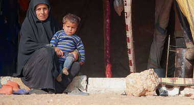 Eine Frau sitzt auf einer Stufe vor einem Zelt. Auf ihrem Schoß sitzt ein Kind.