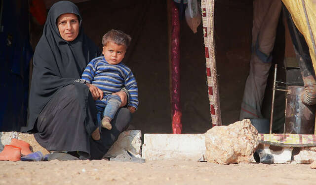 Eine Frau sitzt auf einer Stufe vor einem Zelt. Auf ihrem Schoß sitzt ein Kind.