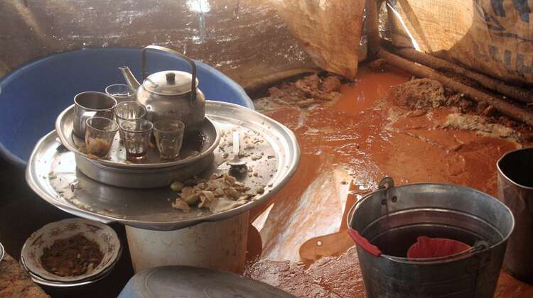 Ein Teegedeck und leere Tabletts mit Essensresten im Inneren eines Zeltes. Der Boden ist sehr matschig und voller Pfützen.