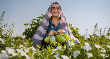Frau sitzt in einem Feld und hält Obst in der Hand.