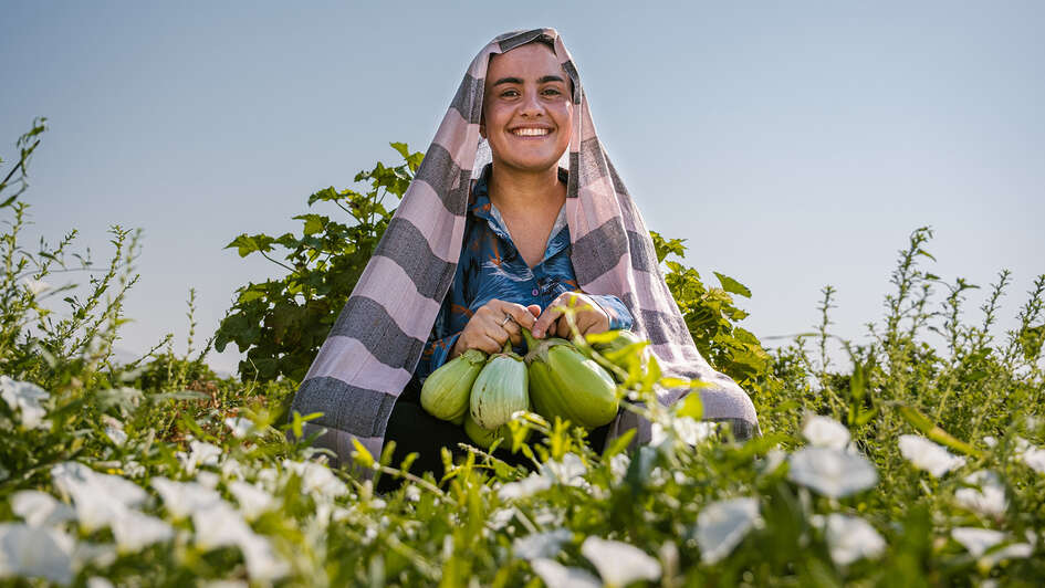 Frau sitzt in einem Feld und hält Obst in der Hand.
