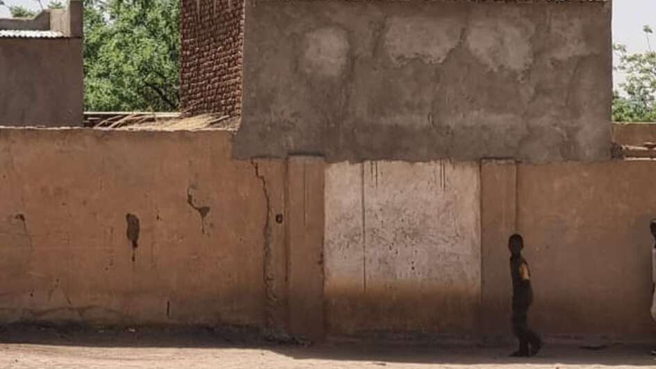 Kind steht vor einem Haus im Sudan nach Ausbruch des Krieges, es steigt Rauch auf.