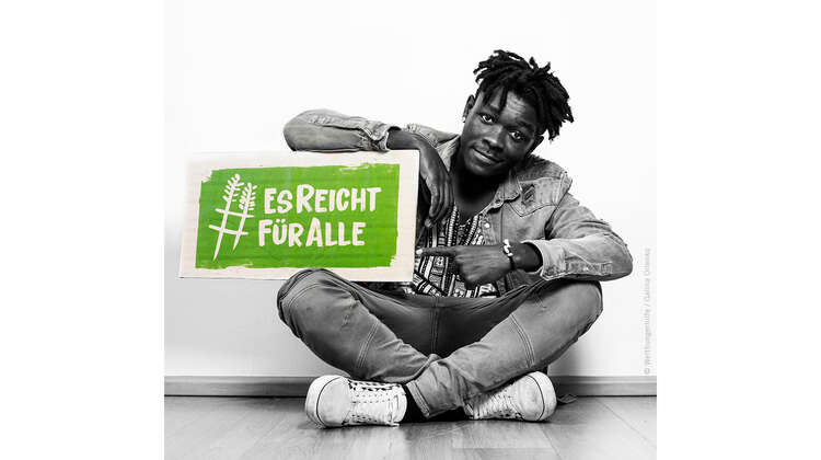 Der Musiker Melchi hält ein Schild mit dem Welthungerhilfe-Hashtag #EsReichtFürAlle.