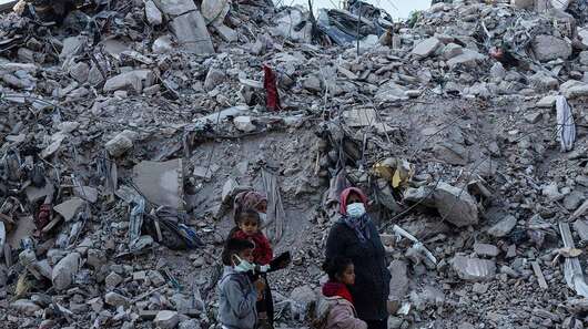 Eine Familie im türkischen Hatay steht nach den Erdbeben 2023 vor großen Trümmerbergen.