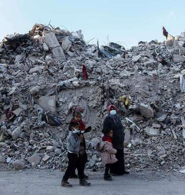 Eine Familie im türkischen Hatay steht nach den Erdbeben 2023 vor großen Trümmerbergen.