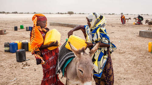 Zwei Frauen heben gelbe Kanister auf einen Esel.