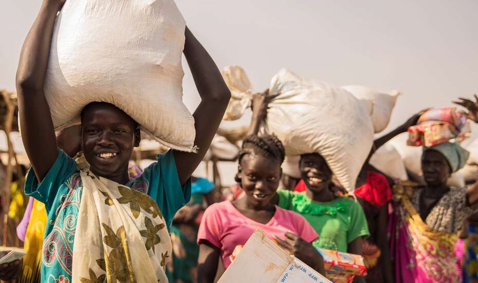 Frauen mit großen Plastiksäcken auf ihren Köpfen, vermutlich gefüllt mit Nahrungsmittel.