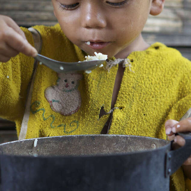 Ein kleiner Junge isst Reis aus dem Topf