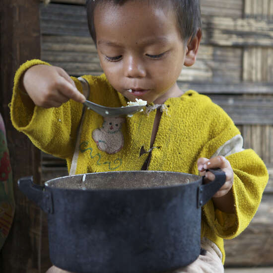 Ein kleiner Junge isst Reis aus dem Topf