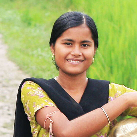 Frau im gelben Sari mit Wasserkrug unter dem Arm