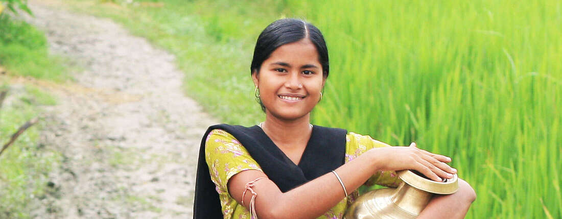 Frau im gelben Sari mit Wasserkrug unter dem Arm