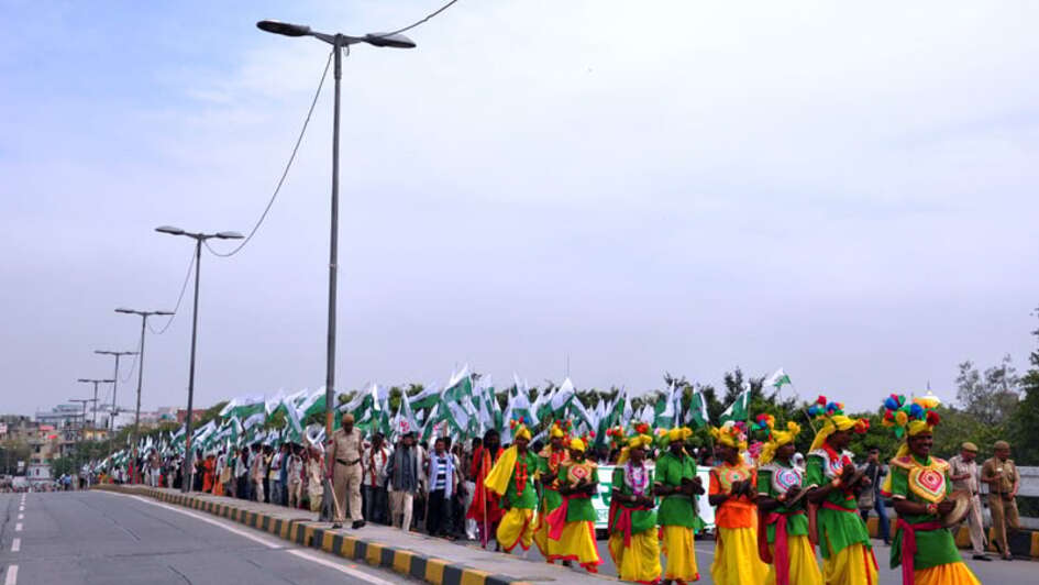 Indigene Demonstranten stehen in tarditionseller Kleidung und mit wehenden Fahnen am Straßrand.